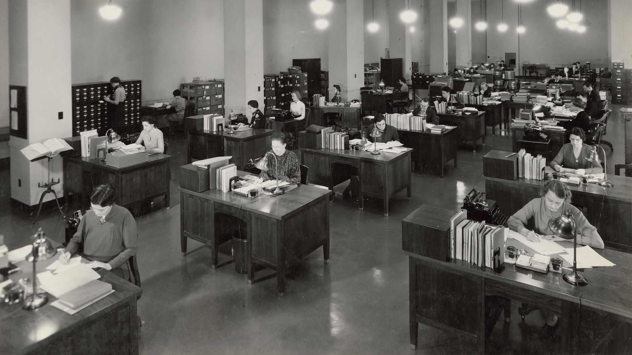 A vintage office pool with people hard at work at their individual desks. Photo from the US National Archives.